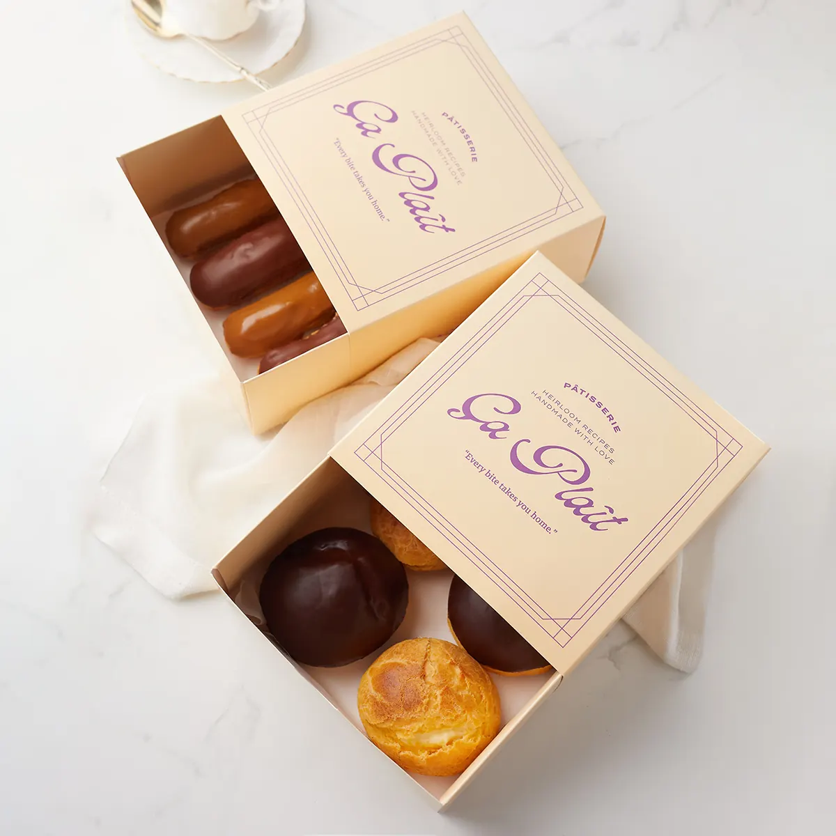 Ça Plaît patisserie in its branded boxes on white marble.