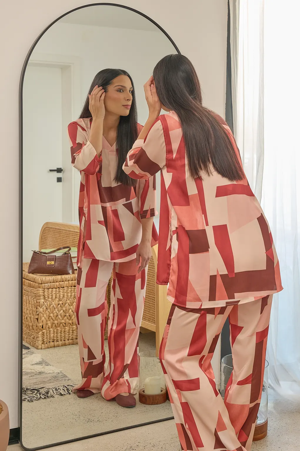 Two women in matching red and cream printed sets at a mirror.