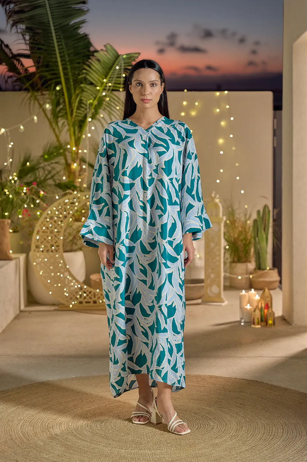 A woman in a printed kaftan on a terrace at dusk.