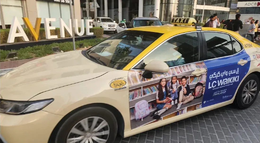 LC Waikiki Back to School artwork on a Dubai taxi outside a mall entrance.