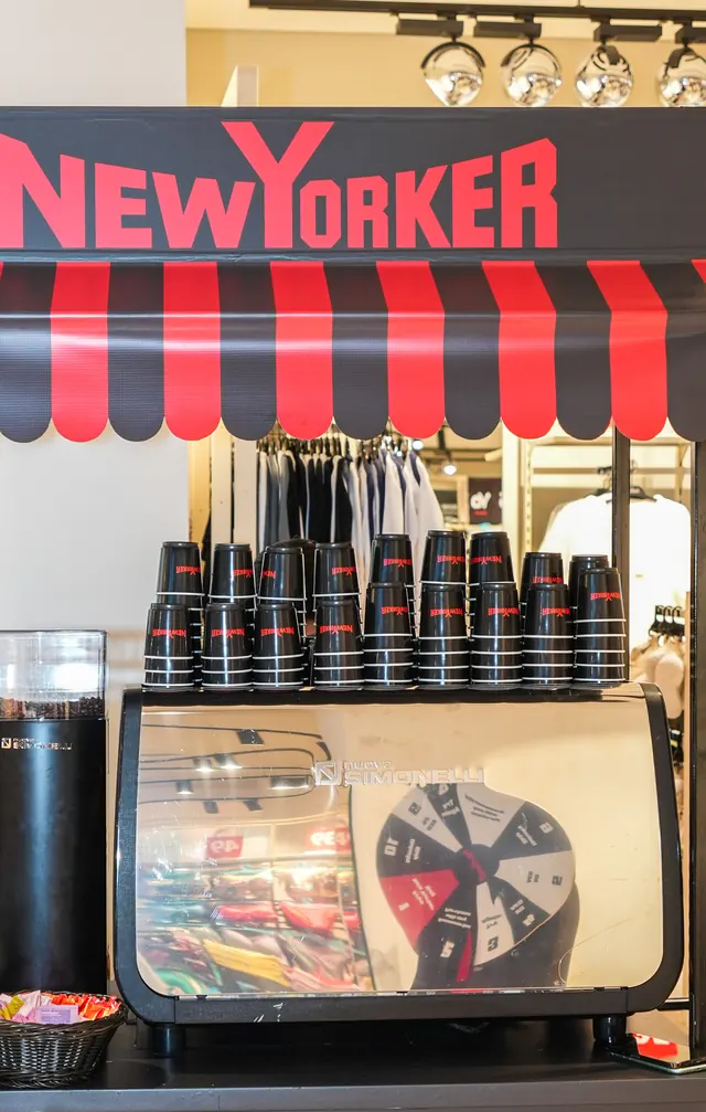 The NEW YORKER coffee cart: the striped awning, the sign and stacks of branded cups above the machine.