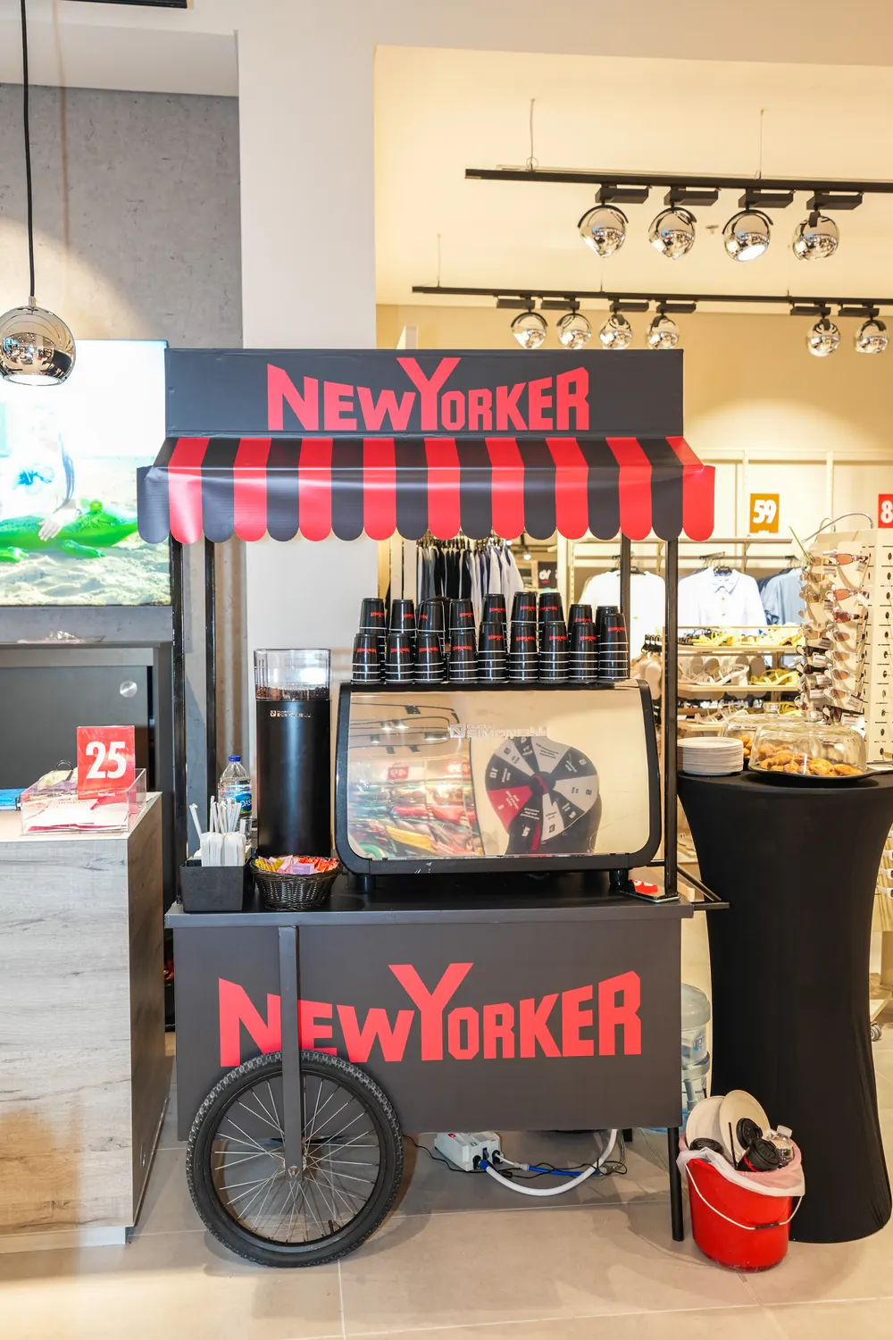 The NEW YORKER coffee cart with a red and black striped awning and branded cups inside the store.