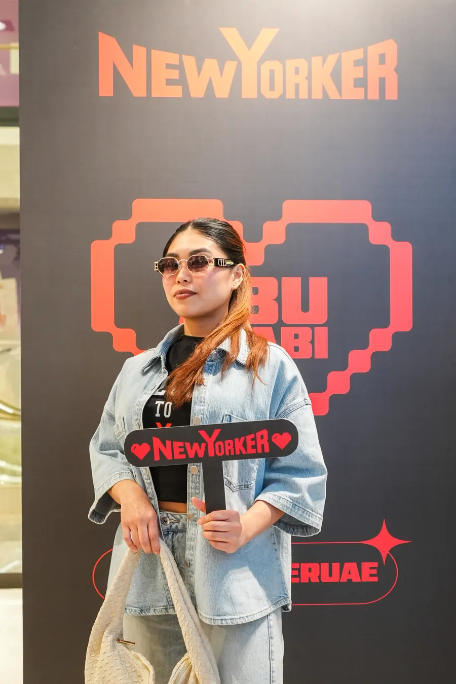 A guest holding a NEW YORKER prop in front of the Abu Dhabi heart photo wall.